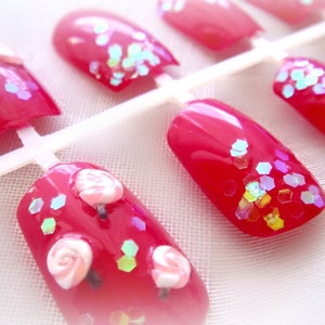 May include: Set of press-on nails in a vibrant red hue, adorned with iridescent glitter and miniature lollipop designs. The nails are attached to a white plastic holder, ready for application. A fun and playful accessory.