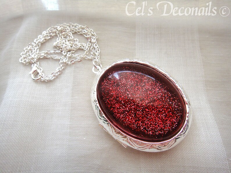 May include: A silver chain necklace with a silver oval locket pendant. The locket has a red glitter design inside.