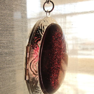 May include: A silver locket necklace with a red glitter filled oval pendant.