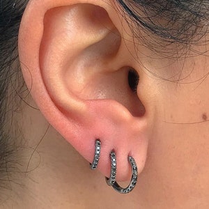 May include: Three black hoop earrings with small black diamonds set in the metal. The earrings are worn in the earlobe.
