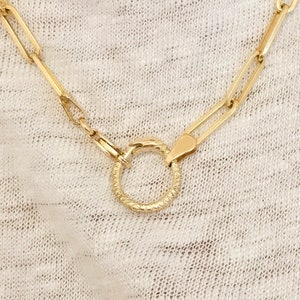 May include: A gold chain necklace with a textured, circular pendant. The chain is made of linked rectangles.