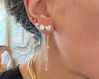 Puede incluir: Primer plano de una oreja adornada con múltiples pendientes de oro. Los pendientes incluyen pequeños pendientes de bola de oro, un elefante de oro, un pendiente de diamante redondo, un pendiente de diamante en forma de corazón y una cadena de oro colgante con pequeños diamantes.