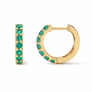 May include: A pair of gold hoop earrings, each featuring a line of bright green gemstones. The earrings are set against a white backdrop, emphasizing the polished gold and the vivid colour of the emerald-style stones.