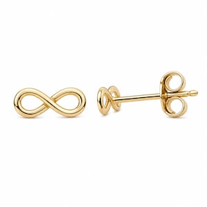 Puede incluir: Un par de pendientes de botón dorados con el símbolo del infinito. Los pendientes se muestran sobre un fondo blanco. El símbolo del infinito es un bucle continuo, y los pendientes tienen un cierre de poste y mariposa.