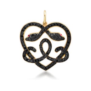 May include: A gold pendant in the shape of a heart, featuring two intertwined snakes. The snakes are outlined with black stones and have red gemstone eyes. The pendant is designed with a loop at the top for a chain.