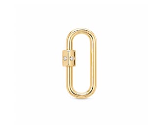 Puede incluir: Un mosquetón ovalado de tono dorado con un mecanismo de cierre rectangular en un lado. El componente de cierre está adornado con dos pequeñas piedras redondas y transparentes engastadas verticalmente en la superficie de metal pulido.