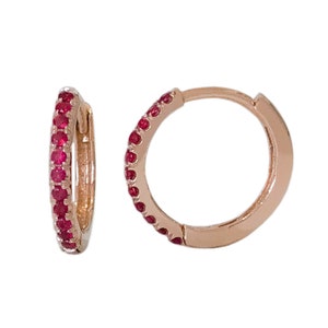 May include: A pair of rose gold hoop earrings with a single row of red gemstones around the edge.