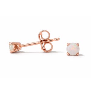 May include: A pair of rose gold stud earrings with a round, white opal gemstone. One earring is shown as a stud, and the other is shown as a stud with the post and backing. The earrings are set against a white background.