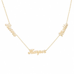 Puede incluir: Un collar de tono dorado que presenta tres colgantes con nombres integrados en una cadena fina. Los nombres Reeves, Harper y Maide están escritos en una fuente cursiva, con Reeves y Maide posicionados a los lados y Harper en el centro.