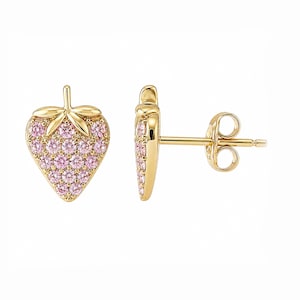 May include: A pair of gold-colored stud earrings shaped like strawberries. The strawberry bodies are covered in small, pink gemstones, while the leaves and stems are gold. The earrings are displayed on a white background.