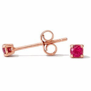May include: A pair of rose gold stud earrings with square, vibrant red gemstones. One earring is shown from the side, displaying the post and butterfly backing. The other earring is shown face-on, showcasing the gemstone's color and setting. Jewelry.