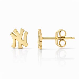 May include: A pair of gold-colored stud earrings. Each earring features the stylized interlocking "NY" logo. The earrings are displayed on a white background, with one earring facing forward and the other showing the post and backing.
