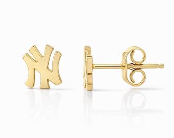 May include: A pair of gold-colored stud earrings. Each earring features the stylized interlocking "NY" logo. The earrings are displayed on a white background, with one earring facing forward and the other showing the post and backing.