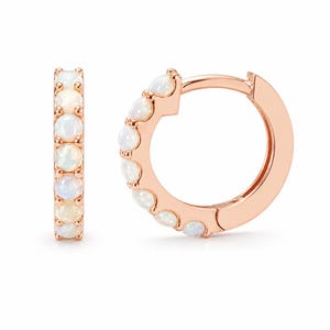 May include: A pair of rose gold hoop earrings featuring a row of small, round, iridescent white opals set along the front curve of each hoop. The earrings have a hinged closure mechanism and a polished metallic finish on the rose gold bands.