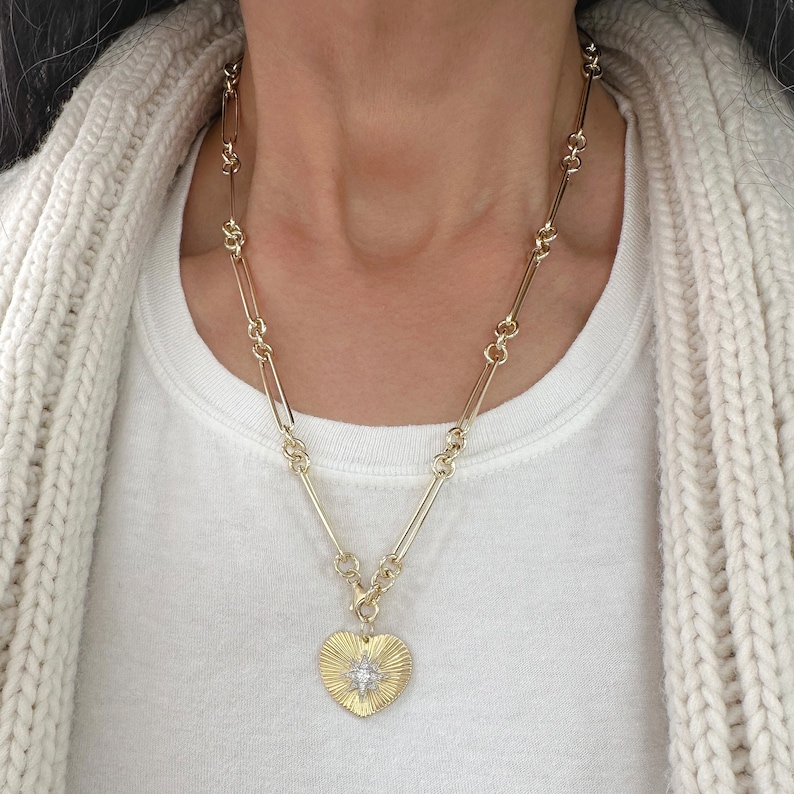 May include: A gold chain necklace with a heart-shaped pendant featuring a starburst design with clear stones.