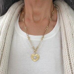 May include: A gold chain necklace with a heart-shaped pendant featuring a starburst design with clear stones.