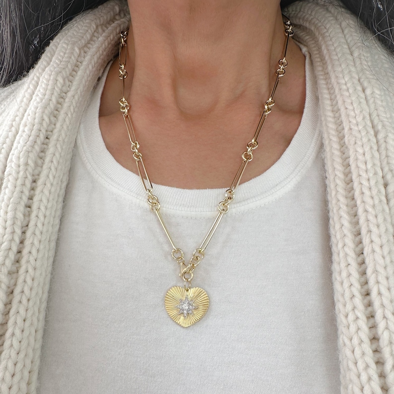 May include: A gold chain necklace with a heart-shaped pendant featuring a starburst design with clear stones.