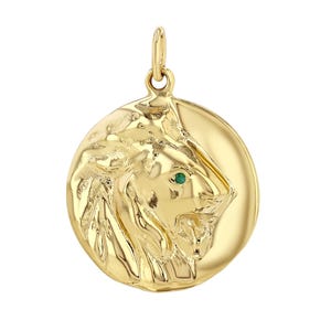 Könnte beinhalten: Ein goldener Löwenkopf-Anhänger mit einem grünen Edelsteinauge. Der Anhänger ist rund und hat ein detailliertes Design.