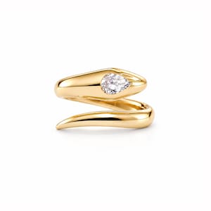 Könnte beinhalten: Ein goldfarbener Wickelring in Form einer gewundenen Schlange mit glatter, polierter Metalloberfläche und einem einzelnen, birnenförmigen, klaren Edelstein, der in den Kopf des Schlangendesigns eingefasst ist und ein schlichtes Schmuckstück bildet.