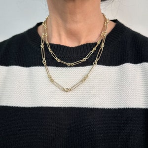 May include: Two gold chain necklaces layered on a person wearing a black and white striped jumper. The chains are made of linked oval shapes.