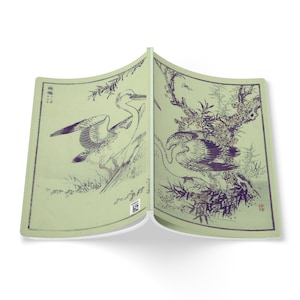 Peut inclure: Un livre ouvert avec des illustrations de style japonais d'oiseaux et de feuillage. Les pages sont vert pâle, avec des illustrations en nuances de gris et de noir. Le livre est ouvert, affichant deux images distinctes d'oiseaux.