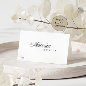 May include: A white folded place card featuring the name Mercedes Hernandez in a black script and sans-serif font, with the text TABLE 1 printed in the bottom left corner. A circular beige sticker reads AVERY & SIGEL COMPATIBLE.