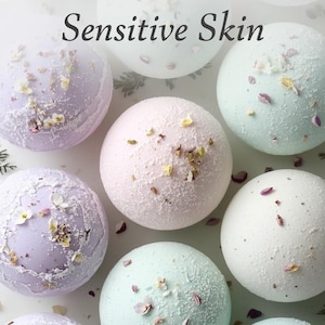 May include: An overhead shot of several round bath bombs in various pastel colors, including lavender, pink, and mint green. The bath bombs are decorated with dried flowers and the text "NATURAL BATH BOMBS Sensitive Skin" is displayed at the top.