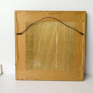 May include: Back of a framed artwork. The frame is a light brown color with a dark brown wire for hanging. The artwork backing is a light brown wood grain.