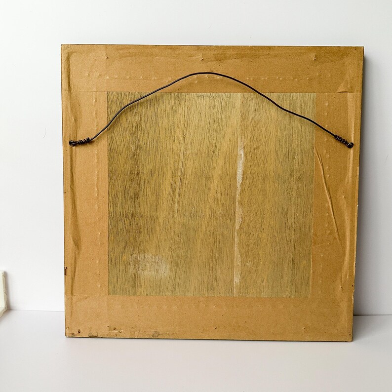 May include: Back of a framed artwork. The frame is a light brown color with a dark brown wire for hanging. The artwork backing is a light brown wood grain.