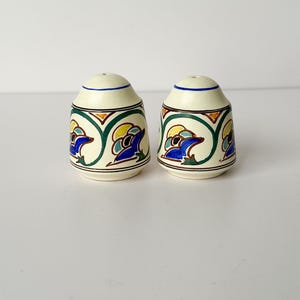 May include: A pair of ceramic salt and pepper shakers. The shakers are off-white with a blue, yellow, and green design. The design features a repeating pattern of stylized birds. The tops of the shakers are blue.