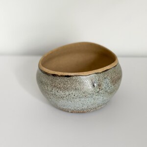 May include: A small, light blue ceramic bowl with a brown rim. The bowl has a speckled, textured surface.