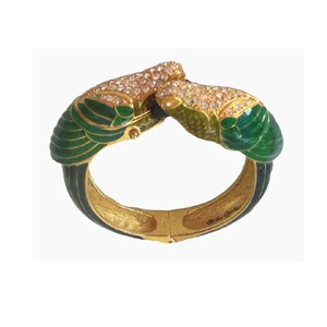 May include: A gold-toned hinged bracelet with green and black enamel accents. The bracelet features two ornate, jeweled parrot heads with clear crystals. The bracelet is a unique piece of jewelry.