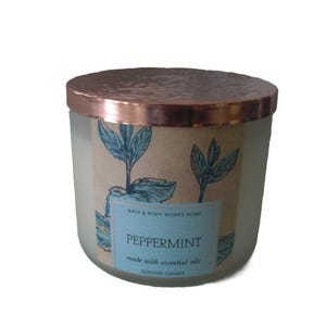 May include: A peppermint-scented candle in a glass jar with a copper-colored lid. The label features blue botanical illustrations and the word "Peppermint". The candle is made with scented oil and soy wax.