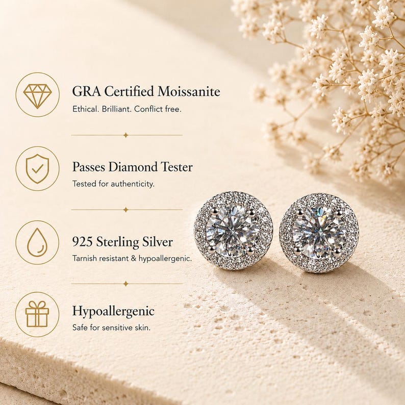 May include: A pair of round, silver-colored stud earrings with a central, sparkling stone surrounded by smaller stones. The earrings are set against a soft, neutral background with text indicating they are GRA certified Moissanite, 925 Sterling Silver, and hypoallergenic.