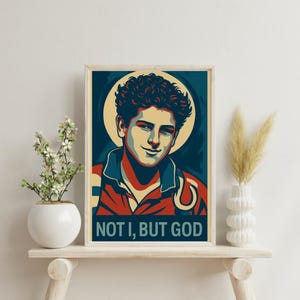 Könnte beinhalten: Ein Vintage-Poster mit dem Porträt eines jungen Mannes mit dunklen Haaren. Das Poster hat ein blaues, rotes und weißes Farbschema und den Text "NOT I, BUT GOD" unten.