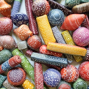 Puede incluir: Surtido de cuentas de cerámica pintadas a mano de varios colores con patrones geométricos. Las cuentas son de diversas formas y tamaños, incluyendo redondas, ovaladas y cilíndricas. Los colores incluyen rojo, naranja, amarillo, verde, azul, morado y marrón.