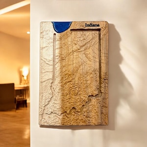 May include: Wooden wall art depicting the state of Indiana. The artwork features a detailed carving of the state's outline, with a blue resin accent representing a body of water. The word "Indiana" is etched at the top.