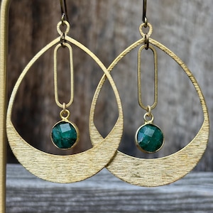 Peut inclure: Une paire de boucles d'oreilles en métal doré brossé avec une grande monture en forme de goutte, un maillon rectangulaire vertical suspendu et une pierre précieuse ronde à facettes vert foncé sertie dans une monture dorée au centre.