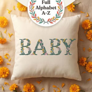Floral embroidery font mockup on cream throw pillow surrounded by golden marigold flowers on linen surface. Word BABY embroidered in botanical teal green letters with yellow and pink blooms. Colorful Full Alphabet A-Z wreath badge overlay. Commercial use OK. 26 letters, 6 sizes 3.5 to 6 inch, 10 formats. PES DST JEF XXX VP3 VIP HUS EXP ART SEW.