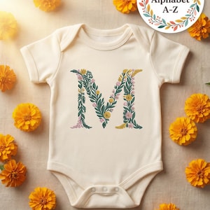 Floral embroidery font mockup on cream baby onesie flat lay surrounded by golden marigold flowers. Large botanical letter M on chest with teal green vines, yellow daisies and pink blooms. Colorful Full Alphabet A-Z wreath badge. Commercial use OK. Perfect for baby nursery gifts. 26 letters, 6 sizes 3.5 to 6 inch, 10 formats. PES DST JEF XXX VP3 VIP HUS EXP ART SEW.