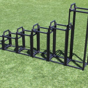 May include: A set of six black metal server racks of varying heights, arranged in ascending order from left to right, on a green artificial grass surface.
