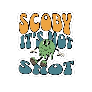 Pode incluir: Um autocolante com o texto "SCOBY IT'S NOT SNOT" em letras de bolhas laranja e azul-petróleo. Uma personagem de desenho animado verde, sorridente, com baba a pingar está no centro. O autocolante tem uma borda branca.