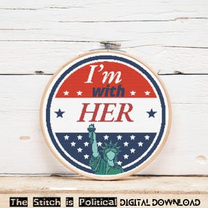 May include: A cross-stitch hoop with a patriotic design. The design features the text "I'm with HER" in red and blue, surrounded by stars and the Statue of Liberty. The text "The Stitch is Political DIGITAL DOWNLOAD" is at the bottom.