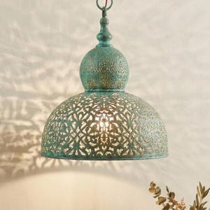 May include: A teal-colored pendant light with a decorative, openwork design. The light fixture is suspended from a chain and casts intricate shadows. The lamp has a dome-shaped shade and a bulbous top, creating an elegant, vintage aesthetic.