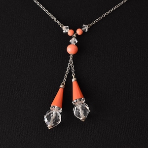 May include: A silver chain necklace with a coral and crystal pendant. The pendant features two teardrop-shaped crystals and a round coral bead.
