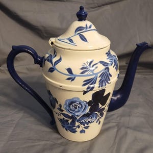 May include: A white ceramic coffee pot with a blue floral design. The pot has a blue lid and a blue handle.