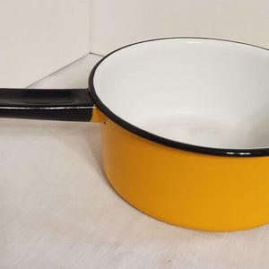 May include: A yellow enamel saucepan with a black handle. The saucepan has a white interior and a black rim.