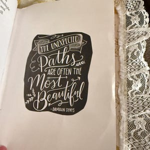 May include: Black and white typography quote on a white background. The quote reads "The unexpected paths are often the most beautiful - Damiaan Denys".