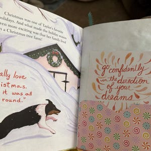 May include: An open book with a page featuring a dog running through the snow towards a house decorated for Christmas. The text on the page reads "I really love Christmas. I wish it was all year round." The opposite page has a pink background with a white card that reads "go confidently in the direction of your dreams".