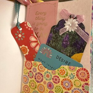 May include: A yellow pocket with a colorful circular pattern. The pocket contains a blue card with a rainbow and the text "what inspires you" and "DESIRE". There is also a pink card with the text "Every thing is going to be okay" and a red bookmark with a floral pattern.